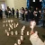 Persone riunite davanti ad una chiesa con candele in mano e striscioni al collo, ascoltano testimonianze di sofferenza e speranza.